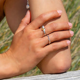 Hand wearing a silver ring with a yellow gemstone, resting on a knee against a natural background.